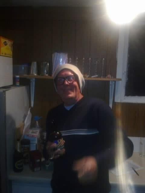 John Wainwright in a beanie and glasses, holding a bottle